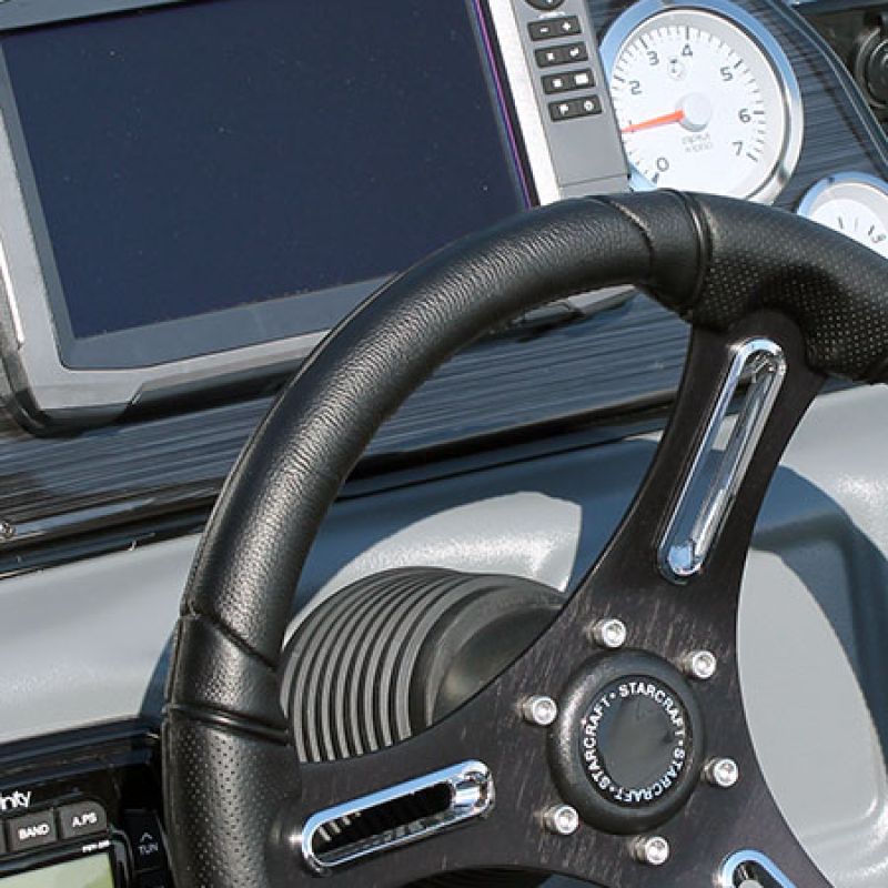 Dashboard of a boat with a leather steering wheel, electronic display, and instrument panel including a tachometer.